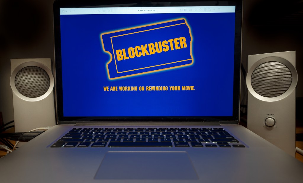 A laptop screen displays the Blockbuster logo with the text, "WE ARE WORKING ON REWINDING YOUR MOVIE."